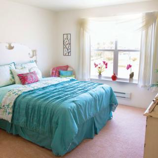 A bright bedroom with turquoise bedding and a large window.