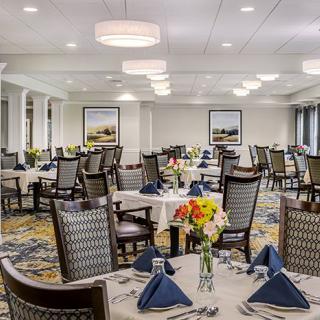 An elegantly set dining room with tables prepared for guests, featuring flowers and neatly folded napkins.