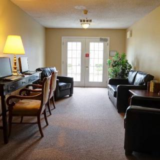 A cozy living room with sofas, chairs, a computer desk, and a lamp, leading to a bright doorway.