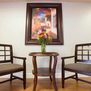A cozy seating arrangement with two chairs and a small table topped with a vase of flowers, framed by a decorative painting.