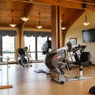 A spacious gym with exercise bikes and modern fitness equipment, featuring a wooden ceiling and large windows.