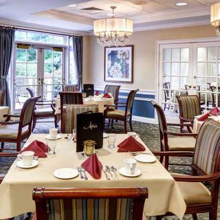 An elegantly set dining room with neatly arranged tables and chairs, featuring chandeliers and tasteful decor.