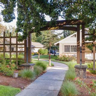 A charming garden pathway leads under an archway towards a house, surrounded by lush greenery and landscaping.