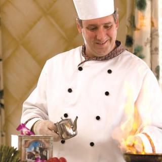A chef in a white uniform skillfully preparing a dish with flames in the kitchen.