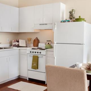 A cozy apartment kitchen with white cabinets, a stove, and a refrigerator.