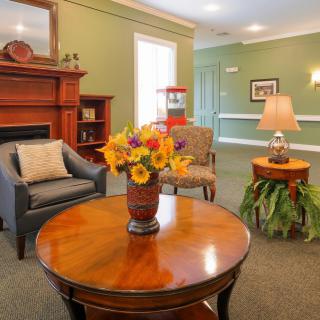 A cozy living room with elegant furniture, featuring a wooden table with a vase of flowers, armchairs, and a fireplace creating a warm atmosphere.
