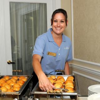 A server in uniform presents a buffet with assorted pastries.