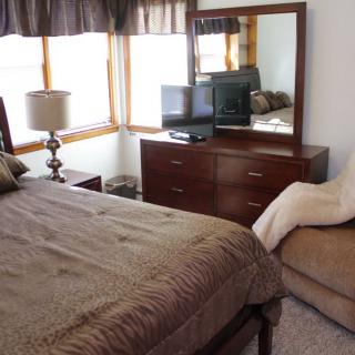 A cozy bedroom featuring a bed, dresser with a mirror, TV, and other furnishings.