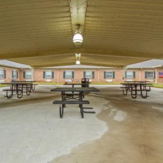 A covered outdoor pavilion with picnic tables surrounded by brick buildings.