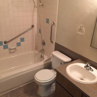 A bathroom with a bathtub, toilet, and sink, featuring grab bars and tiled walls.