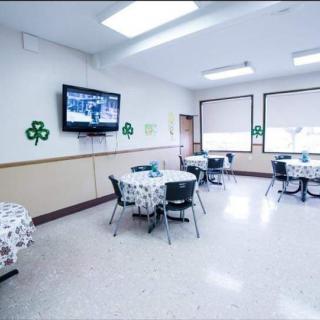 A bright dining room with tables and chairs, featuring a wall-mounted TV and decorative accents.