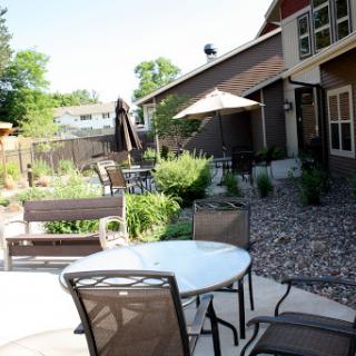 A serene outdoor patio area with a table and chairs, surrounded by lush greenery.