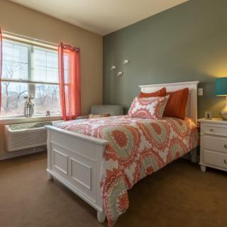 A cozy bedroom featuring a single bed with colorful bedding and a nightstand beside it.