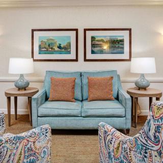 A cozy living room with a blue sofa, patterned chairs, and framed artwork on the wall.