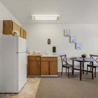 A simple kitchen and dining area with a refrigerator, wooden cabinets, and a small dining table with chairs.