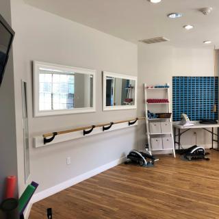 A well-lit exercise studio with mirrors, a ballet barre, and fitness equipment.