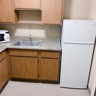 A compact kitchen setup with a refrigerator, wooden cabinets, a sink, and a microwave on the countertop.