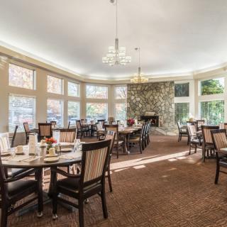 A well-lit dining room with multiple tables and chairs, surrounded by large windows.