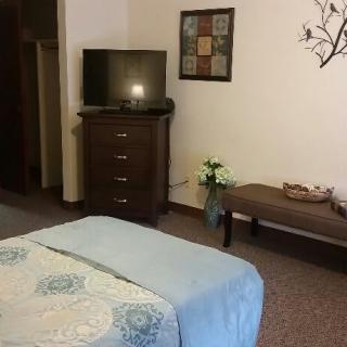 A cozy bedroom featuring a TV on a dresser, a neatly made bed, and a decorative bench with flowers.