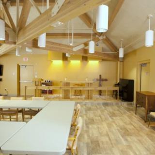 Interior view of a church hall with tables and chairs arranged under wooden beams.