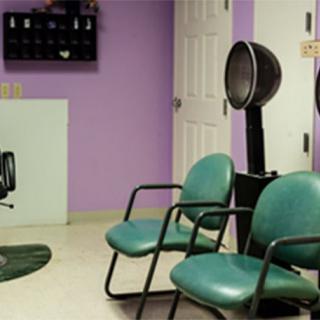 A small salon waiting area with green chairs and a hair dryer against a purple wall.