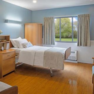 A hospital room with a single bed, wooden furniture, and a large window with curtains.