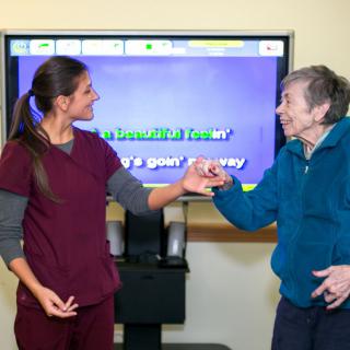A caregiver interacts with a senior woman during a therapy session.