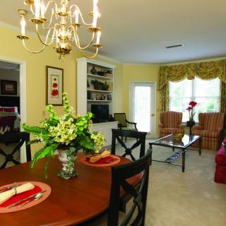A cozy living and dining area with elegant decor, featuring a chandelier and floral centerpiece.