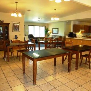 An open dining area with wooden tables and chairs, adjacent to a kitchen, illuminated by overhead lights.