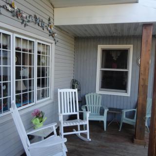 A cozy porch area featuring white rocking chairs, an arrangement of additional seating, and a small flower pot on a wooden deck.