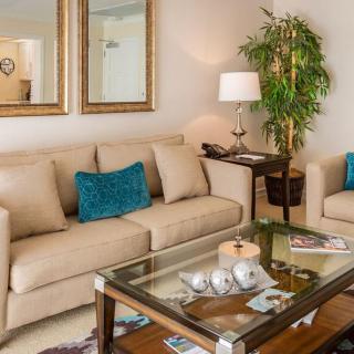 A cozy living room with beige sofas and teal cushions, featuring a glass coffee table and elegant decor.