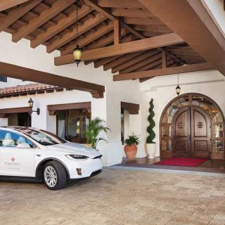 A luxury car parked in front of an elegant building entrance with a wooden door and a covered driveway.