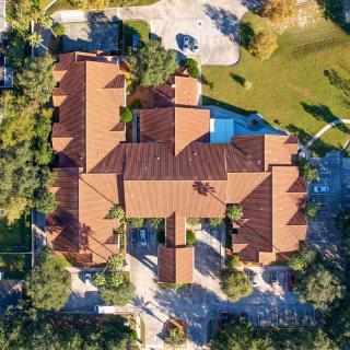 Aerial view of a large house with a red-tiled roof surrounded by trees and a pool.