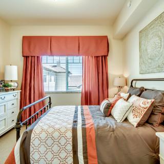 A cozy bedroom with stylish decor and a large window, featuring warm-toned curtains and bedding.