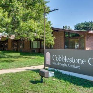Entrance to Cobblestone Crossing community building with a prominent sign and surrounding greenery.
