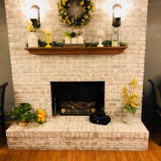 A cozy fireplace adorned with a wooden shelf, decorative plants, and warm lighting.