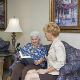 Two women sitting on a couch, engaged in conversation with one holding a book.