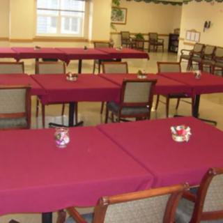 An indoor dining area with tables covered in maroon tablecloths and chairs neatly arranged.