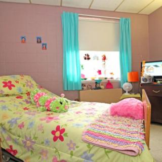 A colorful children's bedroom with floral bedding, turquoise curtains, and pink accents.