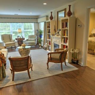 A cozy living room with comfortable seating, bookshelves, and natural light streaming through large windows.