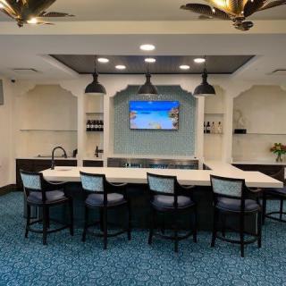 A modern lounge area featuring a bar counter with seating, pendant lighting, and a television.