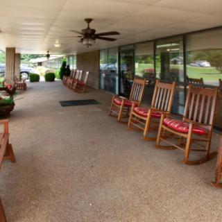 A covered porch with a row of rocking chairs and benches, featuring potted plants for decoration.