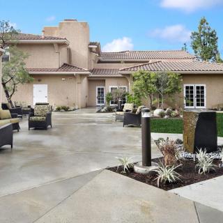 A modern outdoor patio area with seating and landscaping in front of a beige building under a blue sky.