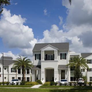 A modern apartment building surrounded by palm trees under a partly cloudy sky.