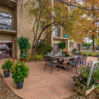 A welcoming outdoor patio area at an apartment complex, featuring a table and chairs surrounded by lush greenery.