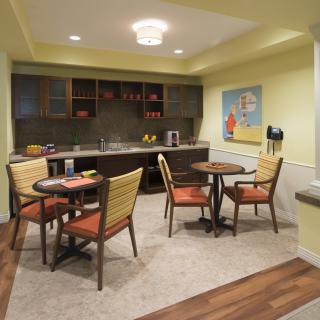 A cozy dining area with a small kitchen space, featuring tables and chairs, warm lighting, and modern decor.