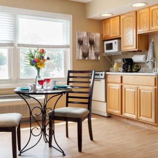 A cozy kitchen with a small dining table and chairs, featuring light wooden cabinets and a large window.