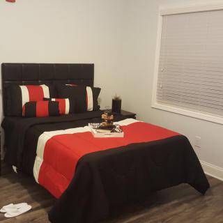 A modern bedroom with a neatly made bed featuring red, black, and white bedding.