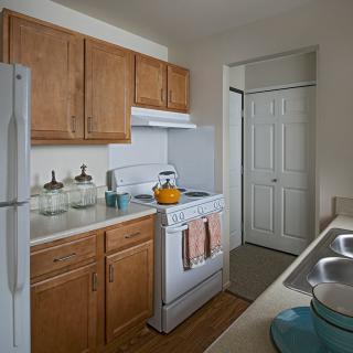 A compact kitchen with wooden cabinets, stove, and refrigerator.