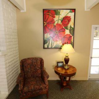 A cozy living room corner featuring a patterned armchair, side table with a lamp, and a vibrant floral painting on the wall.